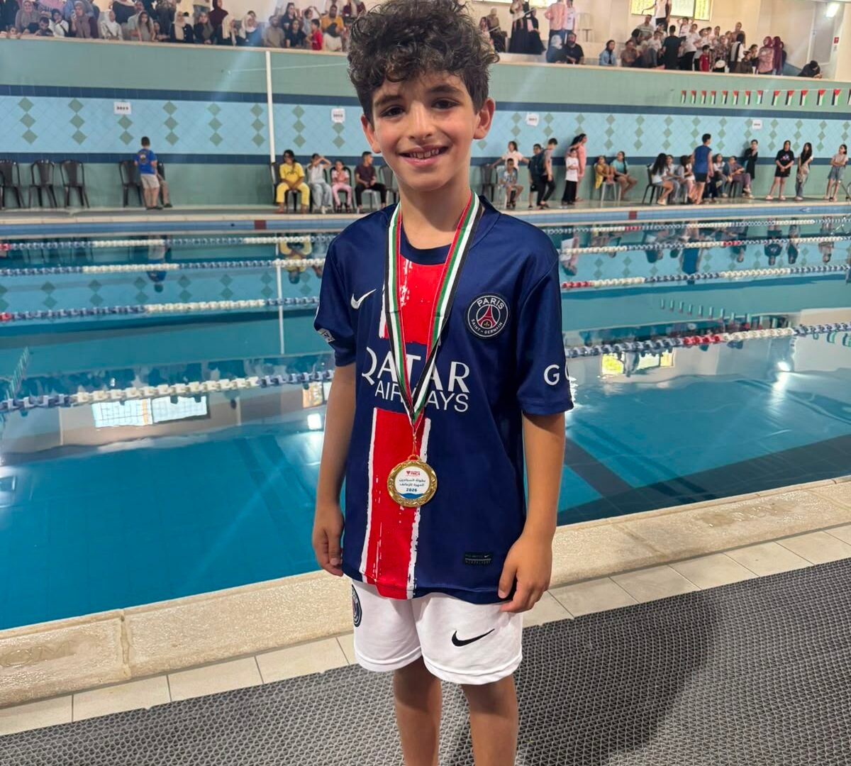 Young De La Salle swimmer wearing a gold medal beside the swimming pool.