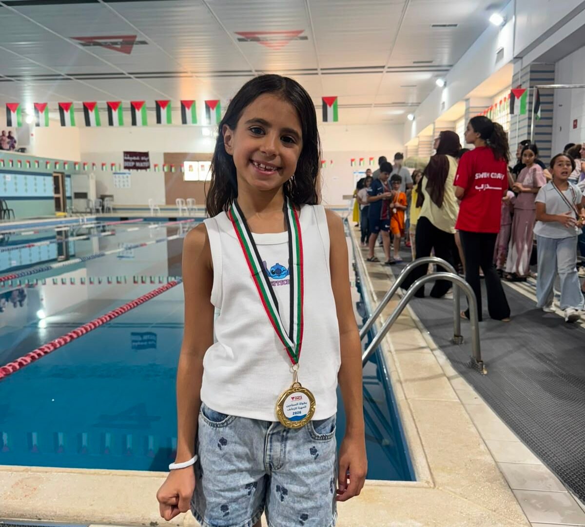 Young medal-winning swimmer standing proudly beside the championship pool.