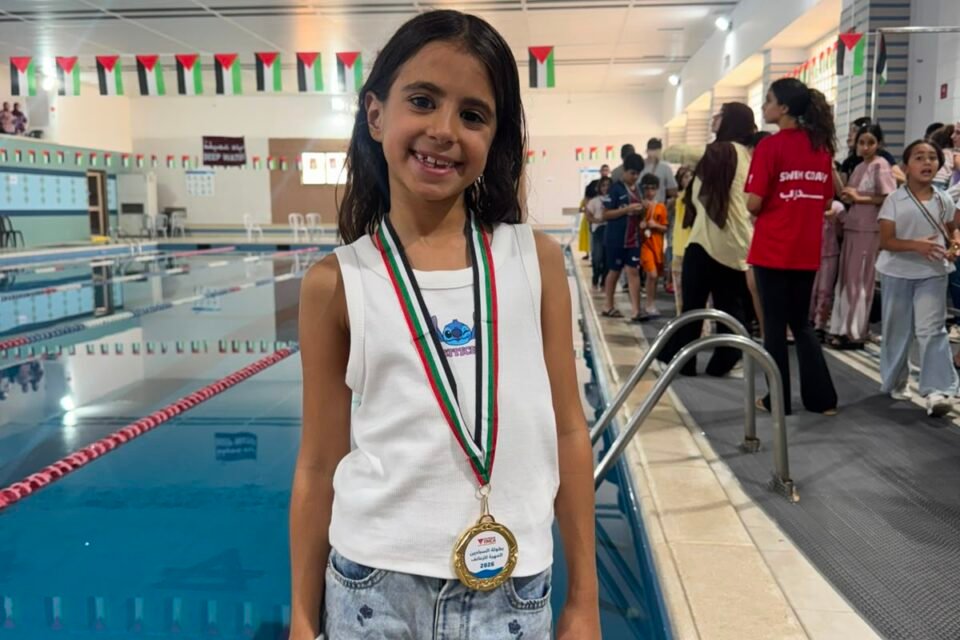 Young medal-winning swimmer standing proudly beside the championship pool.